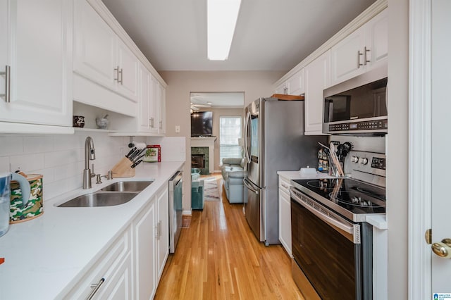 kitchen with sink, backsplash, white cabinets, stainless steel appliances, and light wood-type flooring