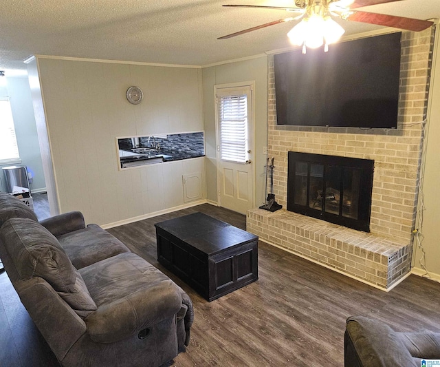 living room featuring hardwood / wood-style floors, ornamental molding, ceiling fan, a brick fireplace, and a textured ceiling