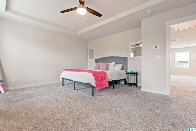 carpeted bedroom with a raised ceiling and ceiling fan