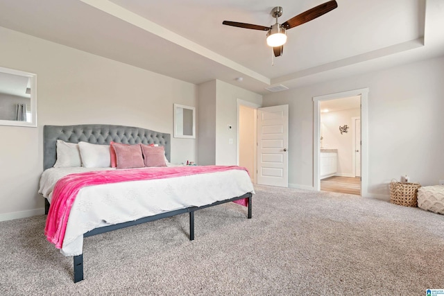 carpeted bedroom featuring a tray ceiling, ensuite bath, and ceiling fan