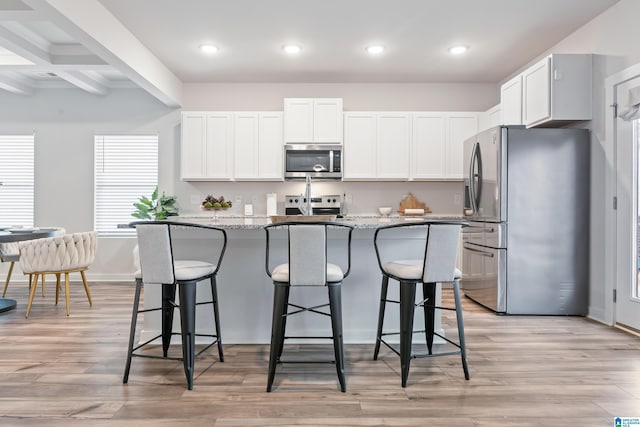 kitchen with appliances with stainless steel finishes, a breakfast bar, white cabinetry, a kitchen island with sink, and light stone countertops