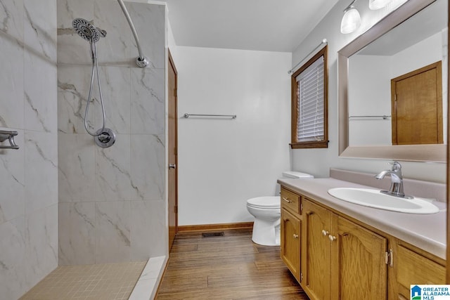 bathroom featuring vanity, toilet, hardwood / wood-style floors, and a tile shower