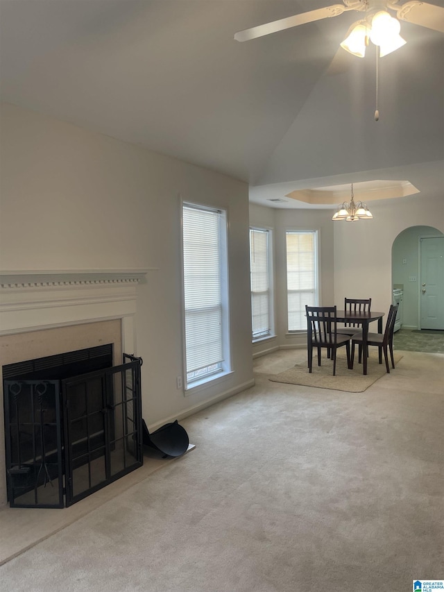 living room with a raised ceiling, carpet flooring, and ceiling fan with notable chandelier