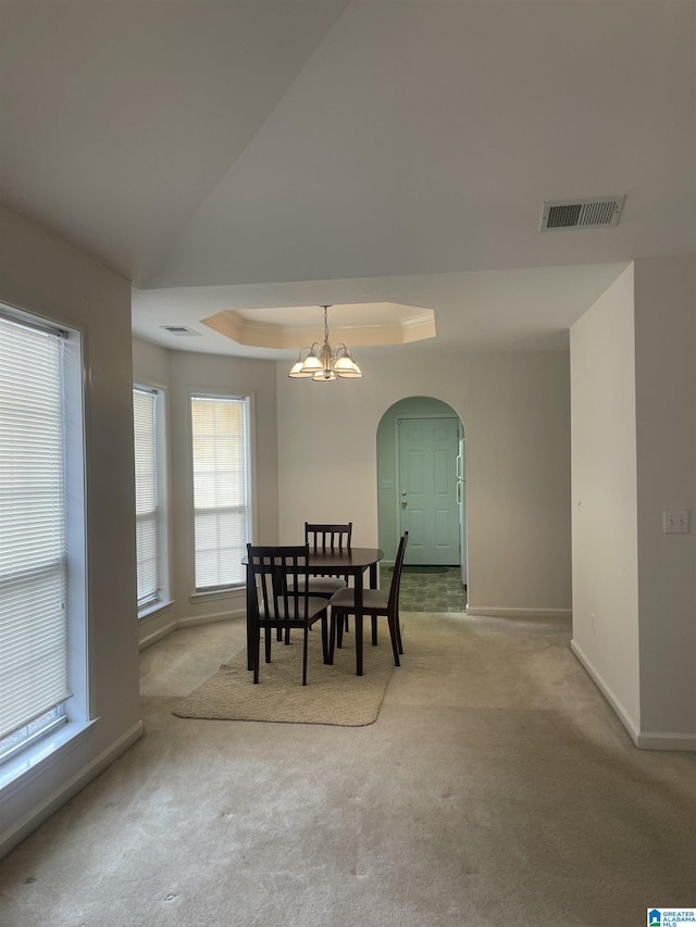 dining area with a tray ceiling, light carpet, and a notable chandelier