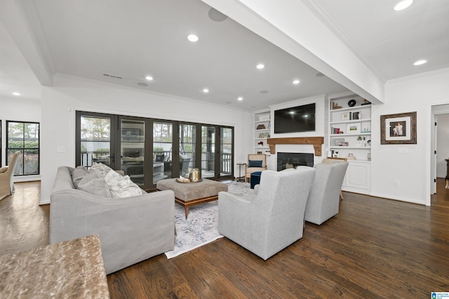 living room featuring dark wood-type flooring, french doors, a large fireplace, ornamental molding, and built in features