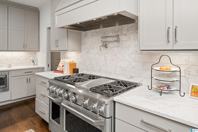 kitchen with light stone counters, tasteful backsplash, double oven range, dark hardwood / wood-style flooring, and custom range hood