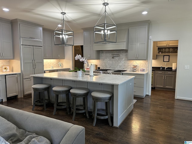 kitchen featuring dark hardwood / wood-style floors, pendant lighting, an island with sink, gray cabinetry, and light stone countertops