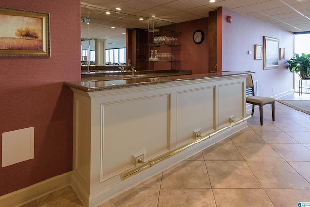 bar with dark stone countertops, a drop ceiling, and light tile patterned floors