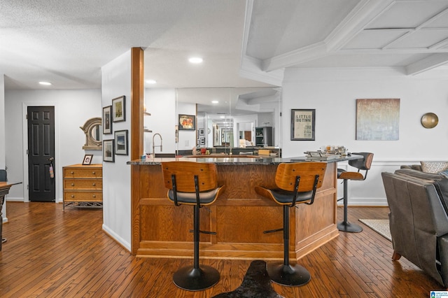 kitchen with a textured ceiling, dark hardwood / wood-style flooring, a kitchen breakfast bar, kitchen peninsula, and beamed ceiling