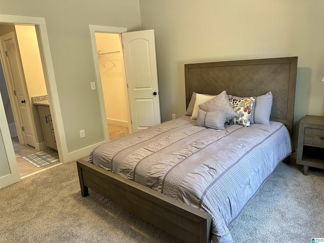 bedroom featuring a spacious closet, light colored carpet, ensuite bath, and a closet