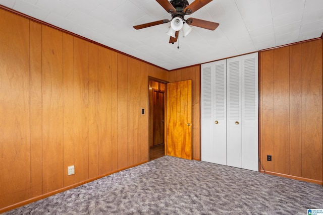 unfurnished bedroom with ceiling fan, carpet floors, and wood walls