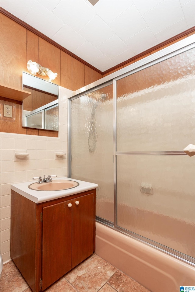 bathroom with ornamental molding, shower / bath combination with glass door, vanity, and tile walls