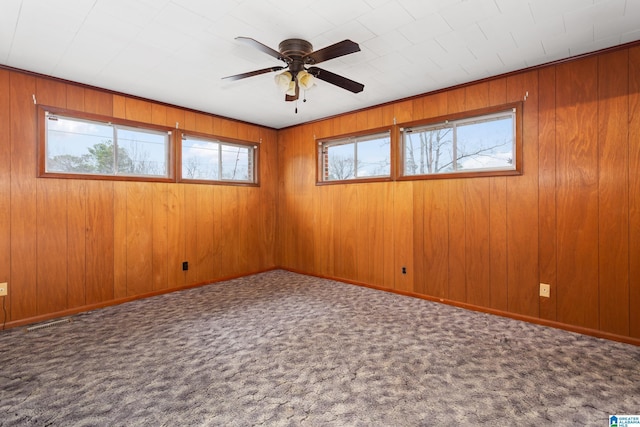 carpeted spare room with wooden walls, a wealth of natural light, and ceiling fan