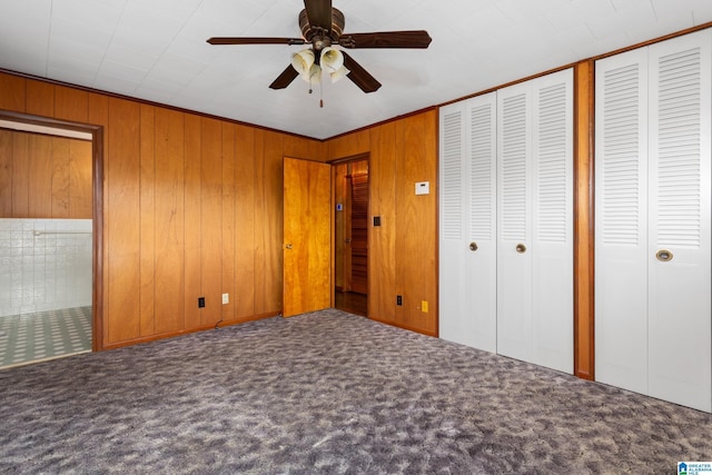 unfurnished bedroom with ceiling fan, carpet floors, two closets, and wooden walls