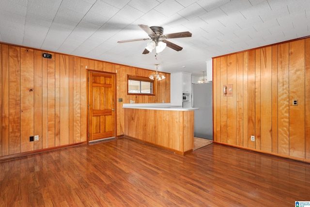 kitchen with built in fridge, ceiling fan with notable chandelier, wooden walls, dark hardwood / wood-style flooring, and kitchen peninsula