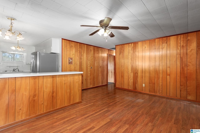 kitchen featuring dark hardwood / wood-style floors, ceiling fan with notable chandelier, stainless steel refrigerator, decorative light fixtures, and kitchen peninsula