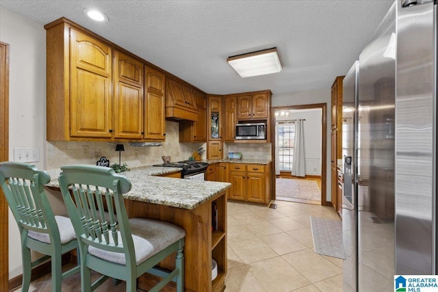 kitchen featuring light tile patterned floors, appliances with stainless steel finishes, tasteful backsplash, light stone countertops, and kitchen peninsula