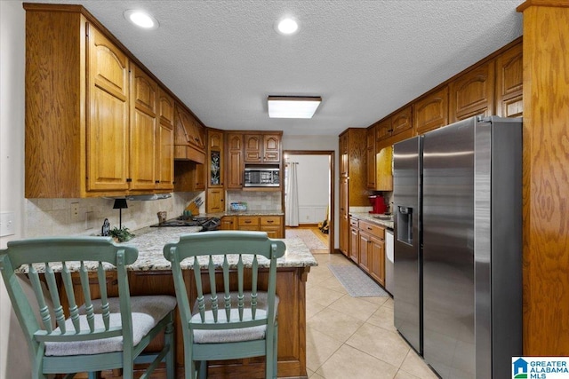 kitchen featuring light tile patterned flooring, tasteful backsplash, a textured ceiling, appliances with stainless steel finishes, and kitchen peninsula