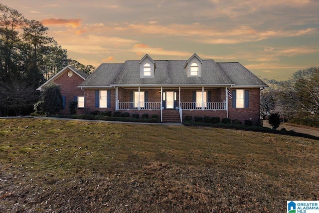 cape cod-style house with a lawn and covered porch