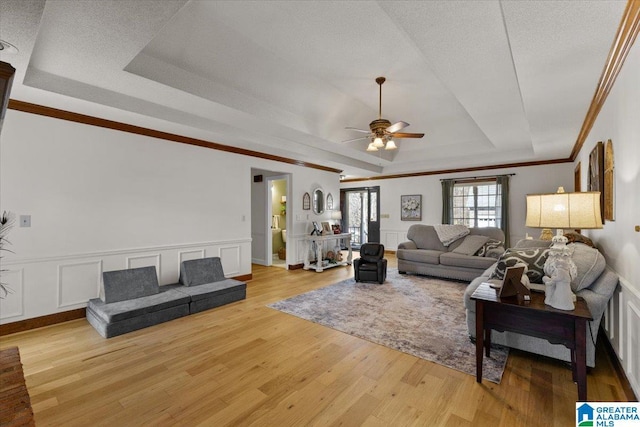 living room featuring crown molding, light hardwood / wood-style floors, a raised ceiling, and a textured ceiling