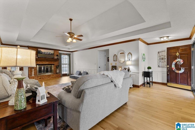 living room with crown molding, a fireplace, a raised ceiling, and light wood-type flooring