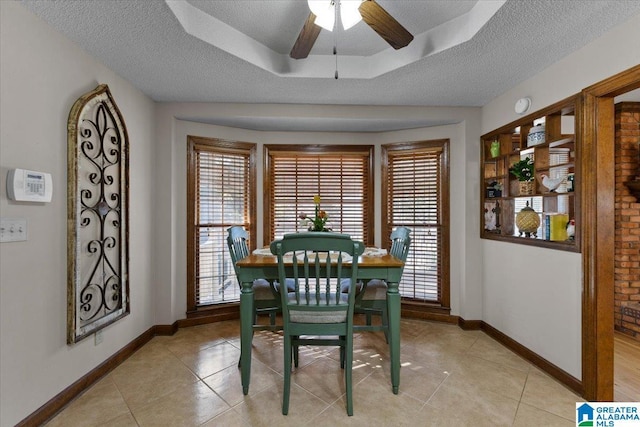 tiled dining space featuring a raised ceiling, ceiling fan, and a textured ceiling