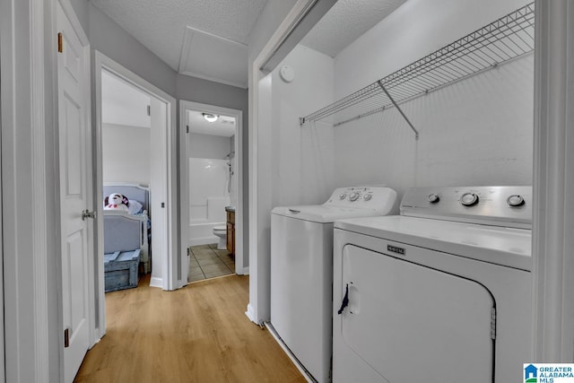 laundry area featuring light hardwood / wood-style flooring, washer and clothes dryer, and a textured ceiling