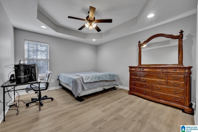 bedroom with ceiling fan, a textured ceiling, light hardwood / wood-style floors, and a tray ceiling