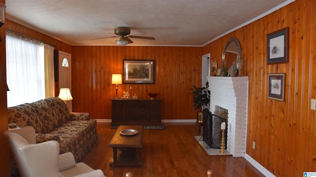 living room featuring ceiling fan, hardwood / wood-style floors, ornamental molding, a brick fireplace, and wood walls