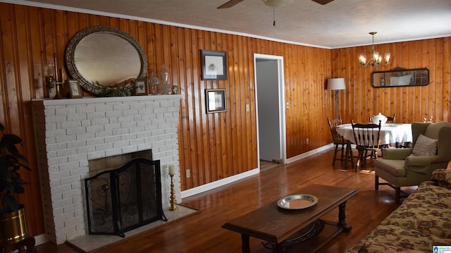 living room featuring crown molding, hardwood / wood-style flooring, a fireplace, ceiling fan with notable chandelier, and wood walls