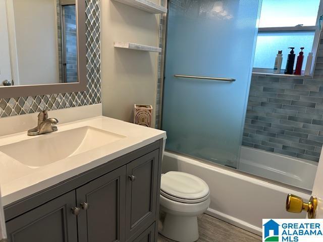 full bathroom with vanity, hardwood / wood-style floors, bath / shower combo with glass door, and toilet