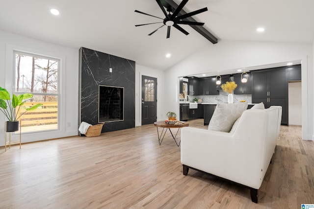 living room featuring vaulted ceiling with beams, ceiling fan, a premium fireplace, and light wood-type flooring