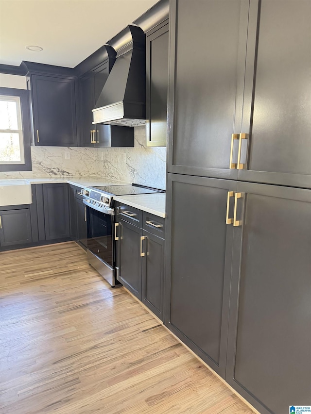 kitchen with backsplash, electric range, light stone countertops, light hardwood / wood-style floors, and custom range hood