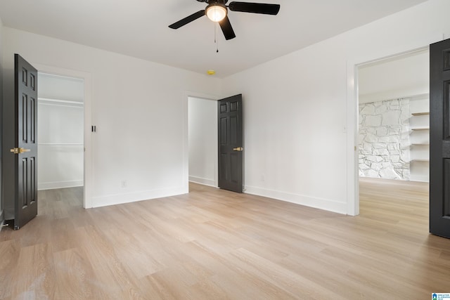 unfurnished bedroom with a walk in closet, light hardwood / wood-style floors, a closet, and ceiling fan