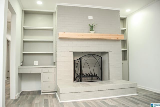 interior details featuring crown molding, built in features, wood-type flooring, built in desk, and a brick fireplace