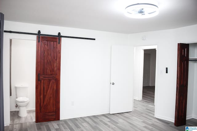 unfurnished bedroom with ensuite bath, a barn door, and light wood-type flooring