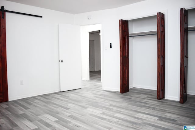 unfurnished bedroom featuring a barn door and light wood-type flooring