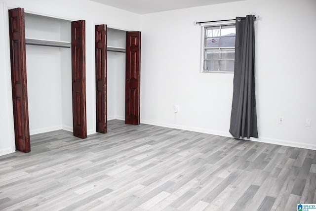 unfurnished bedroom with light hardwood / wood-style flooring and multiple closets