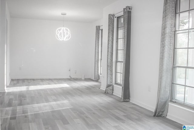 unfurnished room with a notable chandelier and light wood-type flooring