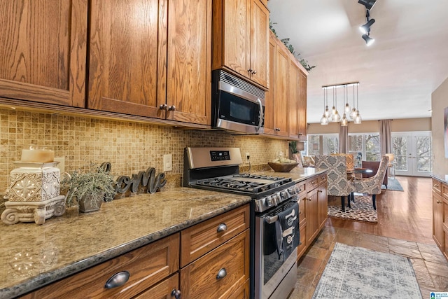 kitchen with hanging light fixtures, a notable chandelier, stainless steel appliances, light stone countertops, and backsplash