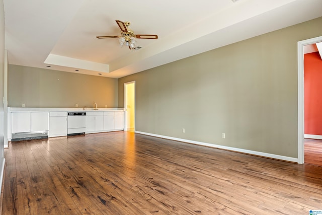 unfurnished living room featuring ceiling fan, sink, a tray ceiling, and hardwood / wood-style floors