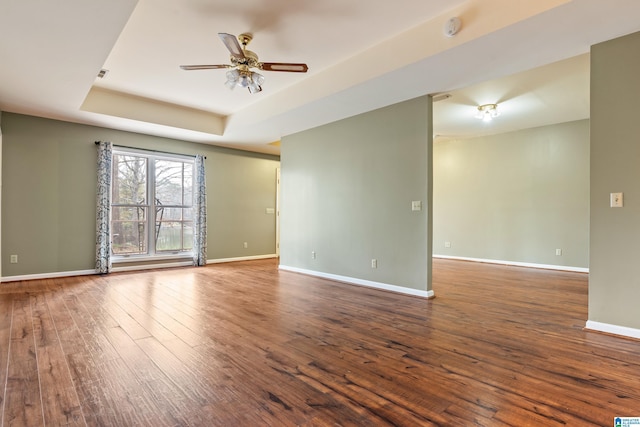 unfurnished room with dark wood-type flooring, ceiling fan, and a tray ceiling