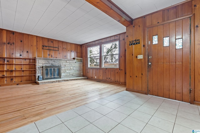 unfurnished living room with beamed ceiling, wooden walls, a stone fireplace, and light hardwood / wood-style floors