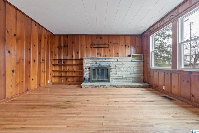 unfurnished living room featuring wooden walls, a fireplace, and light wood-type flooring