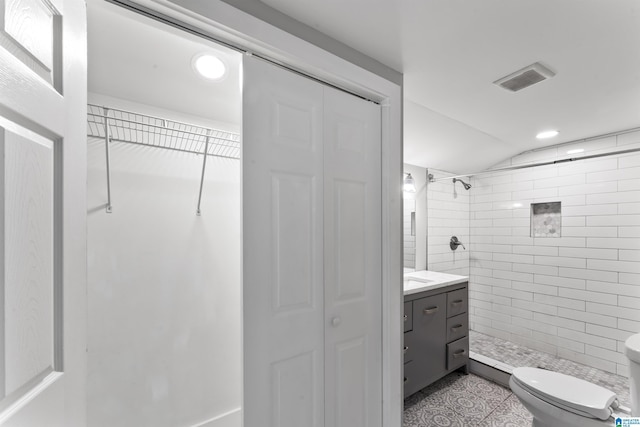 bathroom featuring vanity, lofted ceiling, toilet, and tiled shower