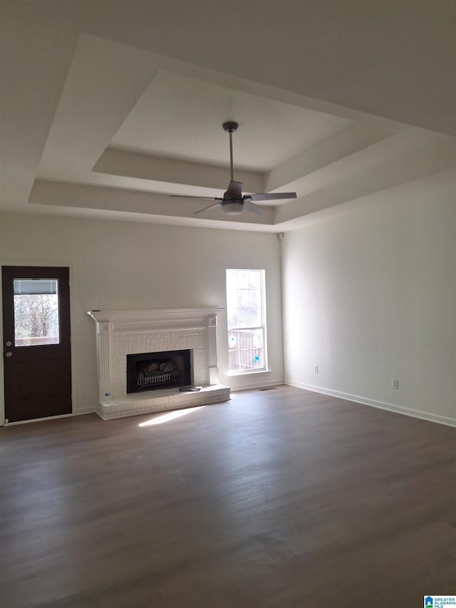 unfurnished living room featuring a healthy amount of sunlight, a tray ceiling, hardwood / wood-style floors, and a brick fireplace