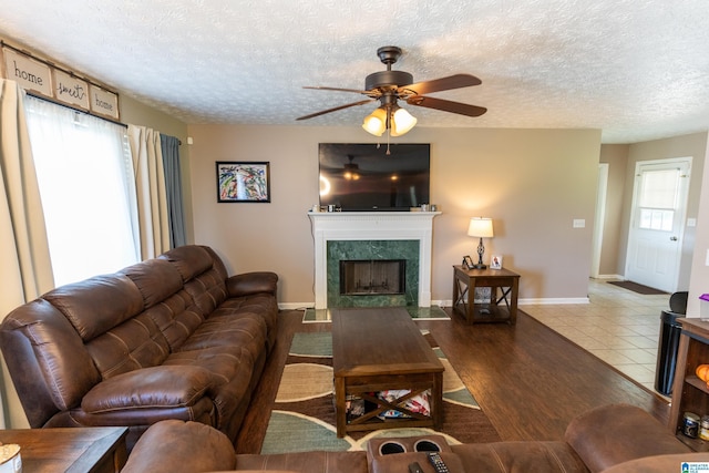 living room featuring ceiling fan, a fireplace, light hardwood / wood-style flooring, and a textured ceiling