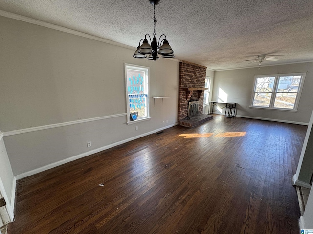 unfurnished living room with crown molding, dark hardwood / wood-style floors, a textured ceiling, a brick fireplace, and ceiling fan with notable chandelier