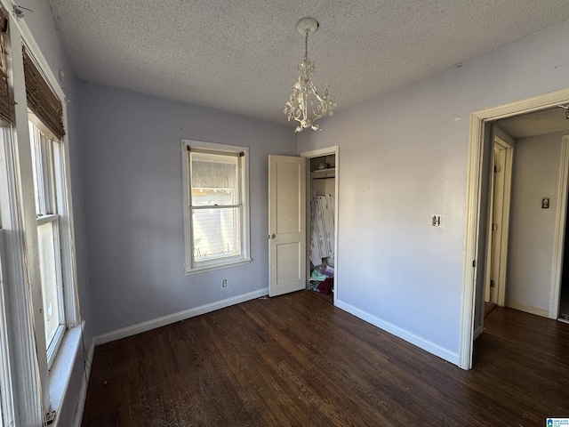 unfurnished bedroom with a notable chandelier, dark wood-type flooring, and a textured ceiling