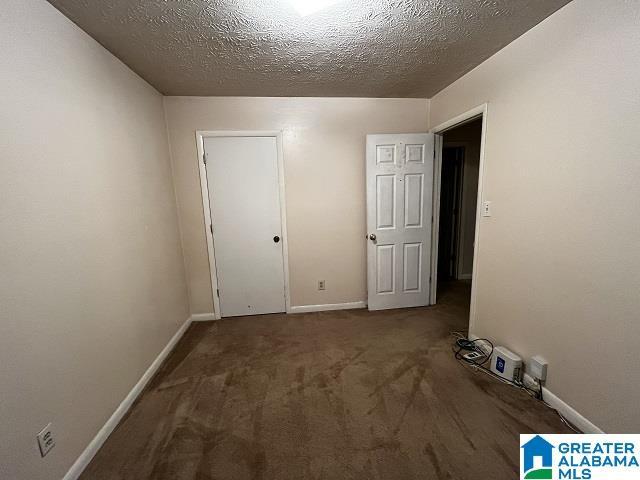 unfurnished bedroom featuring a textured ceiling and dark colored carpet